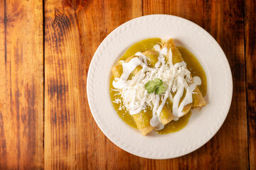 Green enchiladas. Typical Mexican dish made with a folded or rolled corn tortilla filled with shredded chicken and covered with spicy green sauce, cream, grated cheese and onion.