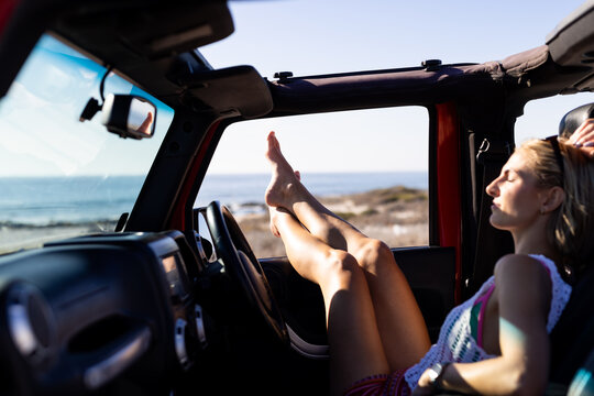 Young Caucasian woman relaxes in a vehicle on a road trip, feet up on the dashboard