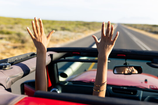 Hands raised in joy during a convertible car ride on a sunny day on a road trip