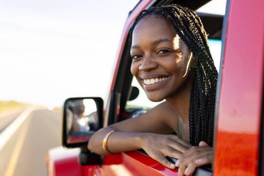 Young African American woman smiles from a red vehicle on a road trip, with copy space