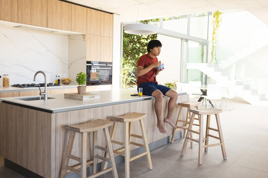 Teenage Asian boy sits casually at a modern kitchen island, with copy space