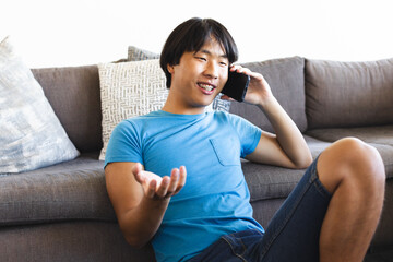 Teenage Asian boy chats on the phone at home, relaxed on a couch