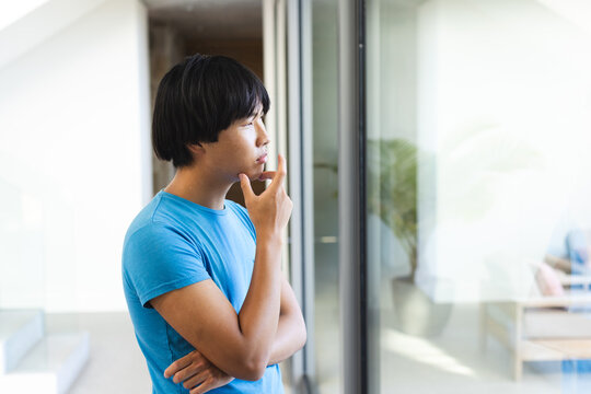 Teenage Asian boy gazes thoughtfully outside a window at home