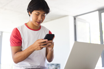 Teenage Asian boy checks his smartphone and laptop in an office setting