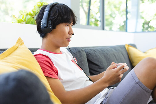 Teenage Asian boy enjoys gaming at home, focused and engaged