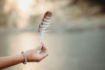 Hand holding feather in the glowing sunlight and water