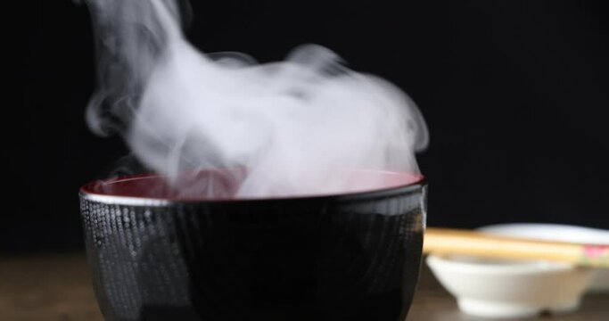 Smoke vape fog rising flowing out of miso soup black red white bowl on dark black background