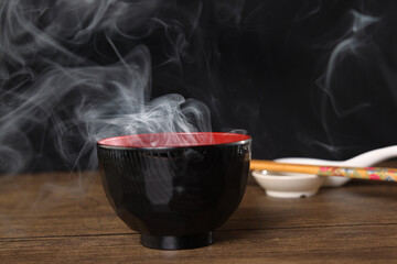 Smoke vape fog rising flowing out of miso soup black red white bowl on dark black background