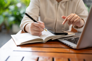 A woman working remotely at a cafe, multitasking with her laptop and phone, and writing in a book.