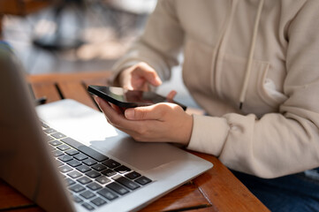 A woman in a white hoodie working remotely at a cafe, multitasking with her smartphone and laptop.