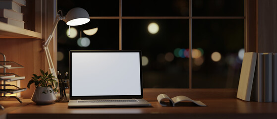 Modern and cozy home office workspace at night with a white-screen laptop computer on a wood table.