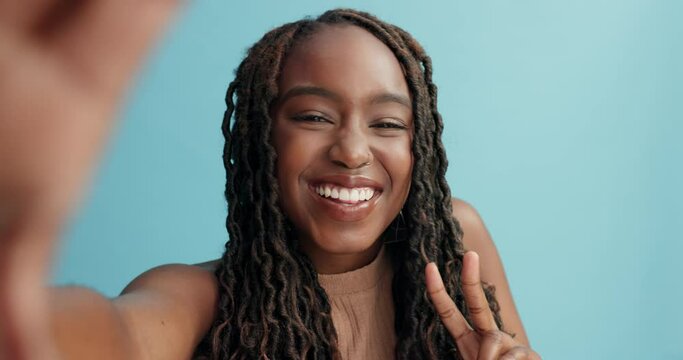 Black woman, face and selfie with happiness, peace hand sign and social media with emoji on blue background. Portrait, influencer and content creation for website, live streaming and V in a studio