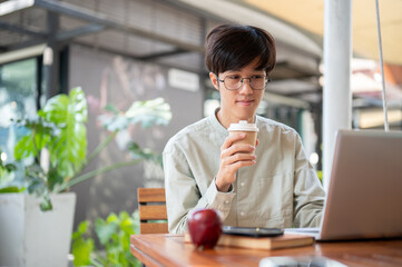 A happy man is sipping coffee and focusing on his work on a laptop, working remotely at a cafe.
