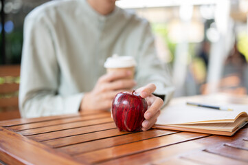 A close-up image of a man holding an apple, eating an apple while relaxing at a cafe.