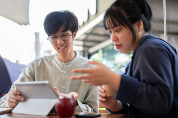 Two young Asian friends or colleagues are discussing and working on a project together at a cafe.