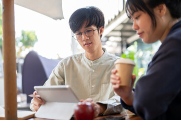 Two young Asian friends or colleagues are discussing and working on a project together at a cafe.