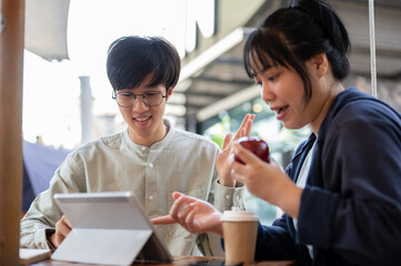 Two young Asian friends or colleagues are discussing and working on a project together at a cafe.