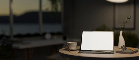 A white-screen digital tablet mockup on a round wooden table in a dark cosy living room at night.