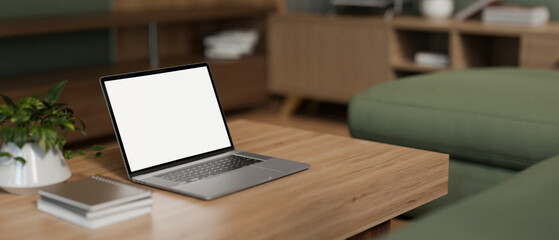 A white-screen laptop computer on a wooden coffee table in a modern and comfortable living room.