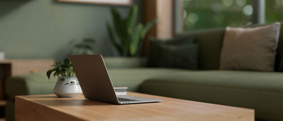 Close-up image of a laptop computer on a wooden coffee table in a modern living room in green color.