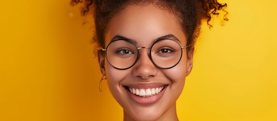 A young woman with glasses is smiling on a yellow background, showcasing her vision care. Her hair frames her face, enhancing her beautiful eyes and eyelashes