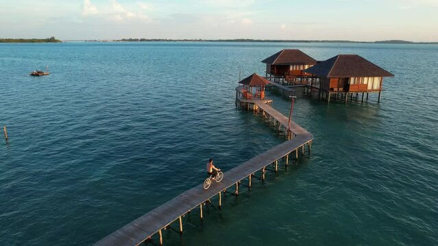 Aerial View of Shirtless Man Riding Bicycle on Wooden Pier Leading to Overwater Exotic Bungalows at Leebong Island, Belitung Indonesia during Sunset