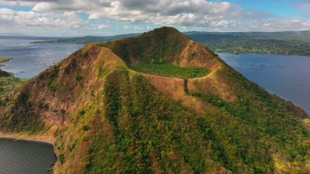 Taal Volcano Crater lighting in sunlight with Taal Lake and Fishing cages in background. Aerial rising tilt down.