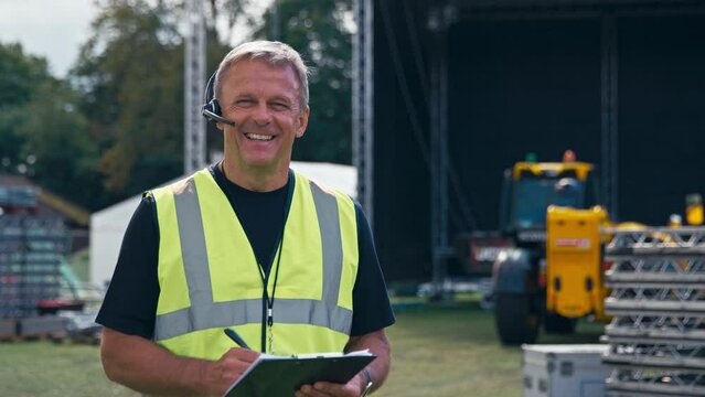 Portrait Of Production Worker With Clipboard Setting Up Outdoor Stage For Music Festival Or Concert