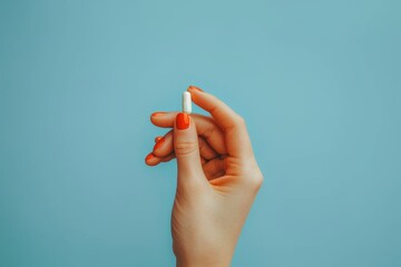 This detailed shot highlights a hand pinching a white pill, with a striking contrast created by the vibrant turquoise blue background