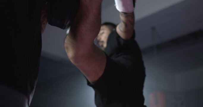 Muay Thai fighter striking a kick into cushioned pad during mitt holder training. Professional martial artist precision blow