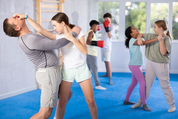 Fototapeta premium Coach man and girl training self-defense techniques in studio..