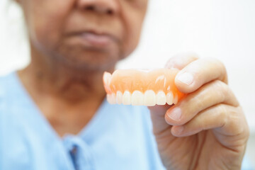 Asian senior woman patient clean teeth denture with toothbrush for chew food.