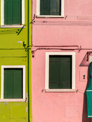 Front view of two old houses in Burano with painted walls, widows blinds, frames, and pipes