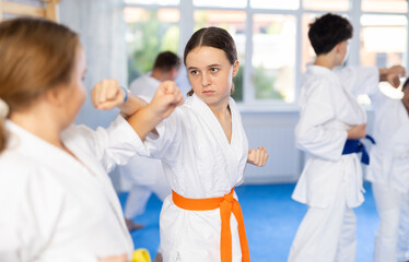 Fototapeta na wymiar Two girls in kimonos train judo techniques in group in studio..