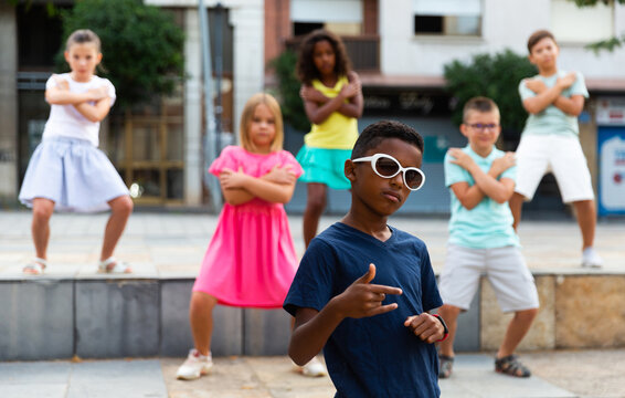 Portrait of confident african boy in sunglasses dancing hip-hop with group of tweens on summer city street..