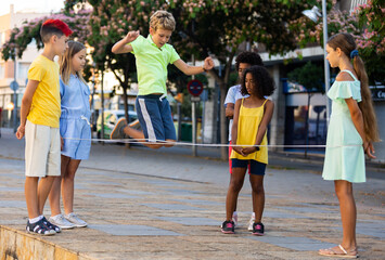 Children active summer games. Interested happy friendly tweenagers playing chinese jump rope in...