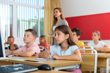 Schoolchildren sitting at desks in classroom. Female teacher staning beside desks.