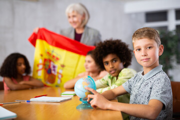 Portrait of a schoolboy in class, studying the history of the country of Spain in lesson and looking for it on the globe