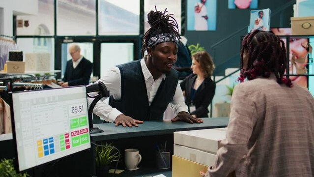African american guy picking up order from clothing store, signing confirmation papers at cash register. Woman employee preparing boxes with requested fashion items and accessories. Camera B.