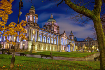 The beautiful City Hall of Belfast illuminated at twilight with some autumnal trees