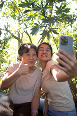 Asian Thai daughter and elder mother taking selfie together with happy smiling, Mom show thumbs up,...
