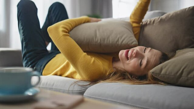 Joyful model falling couch hugging pillow at home closeup. Woman taking phone