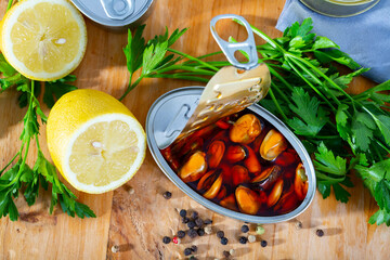 Closeup view of opened can of Spanish style marinated mussels in oil on wooden table with lemon and...