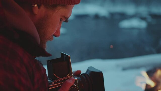 Nature photographer sitting at campsite and focusing camera on bonfire while taking pictures during camping trip in winter