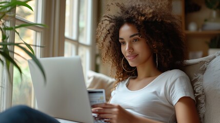 A curly woman sits at a laptop and makes purchases online at home, paying with a bank credit card. Shopping online, season of sales and discounts, best deals. Online store advertising - obrazy, fototapety, plakaty