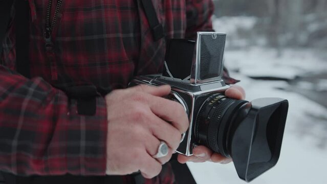Close-up view of hands of professional photographer using digital camera to take picture of nature during winter hike