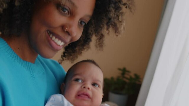 Handheld shot of young beautiful African American woman taking selfie portrait on smartphone with one month old baby son at home