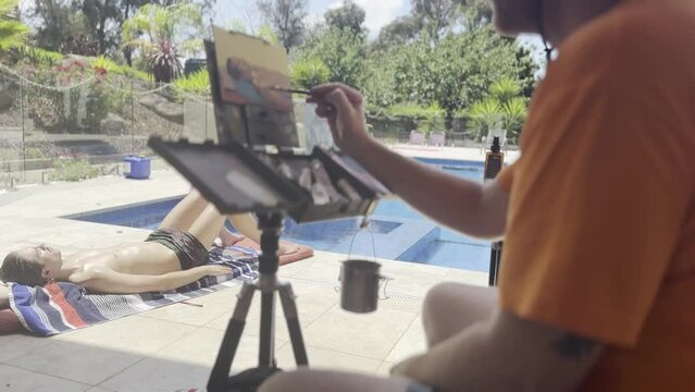 Painter painting young man lying on the edge of swimming pool