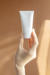 Beautiful female hand holding mock-up of white plastic cream tube in rays of sunlight. Container...