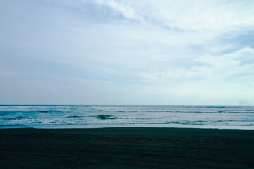 Beautiful beach with a blue sky and black sand and wavy waves